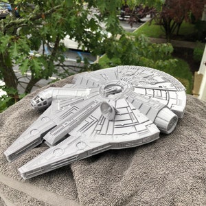 May include: A gray plastic model of the Millennium Falcon spaceship from Star Wars. The model is sitting on a gray towel.