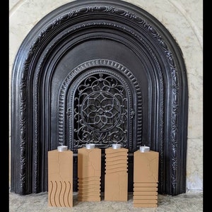 May include: Four brown wooden candle holders with different carved designs, arranged in a row in front of a black fireplace.
