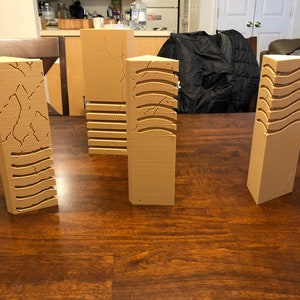 May include: Four brown, rectangular, textured pillars with different patterns. The pillars are made of a smooth, light brown material and have a variety of textures, including cracked, wavy, and striped.