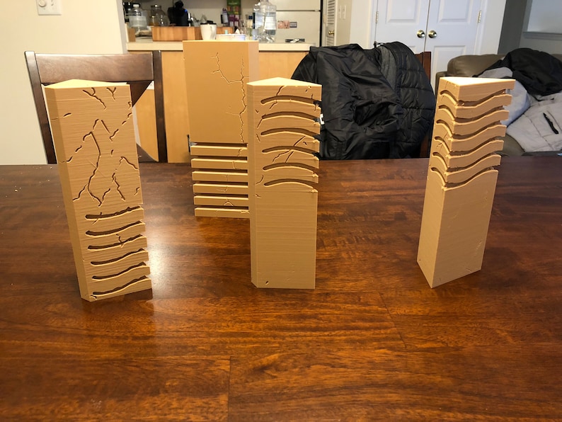 May include: Four brown, rectangular, textured pillars with different patterns. The pillars are made of a smooth, light brown material and have a variety of textures, including cracked, wavy, and striped.