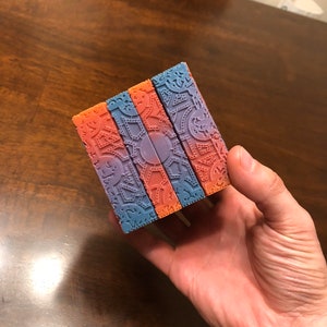 May include: Four bars of soap with a geometric pattern. The soap is a gradient of orange and purple.