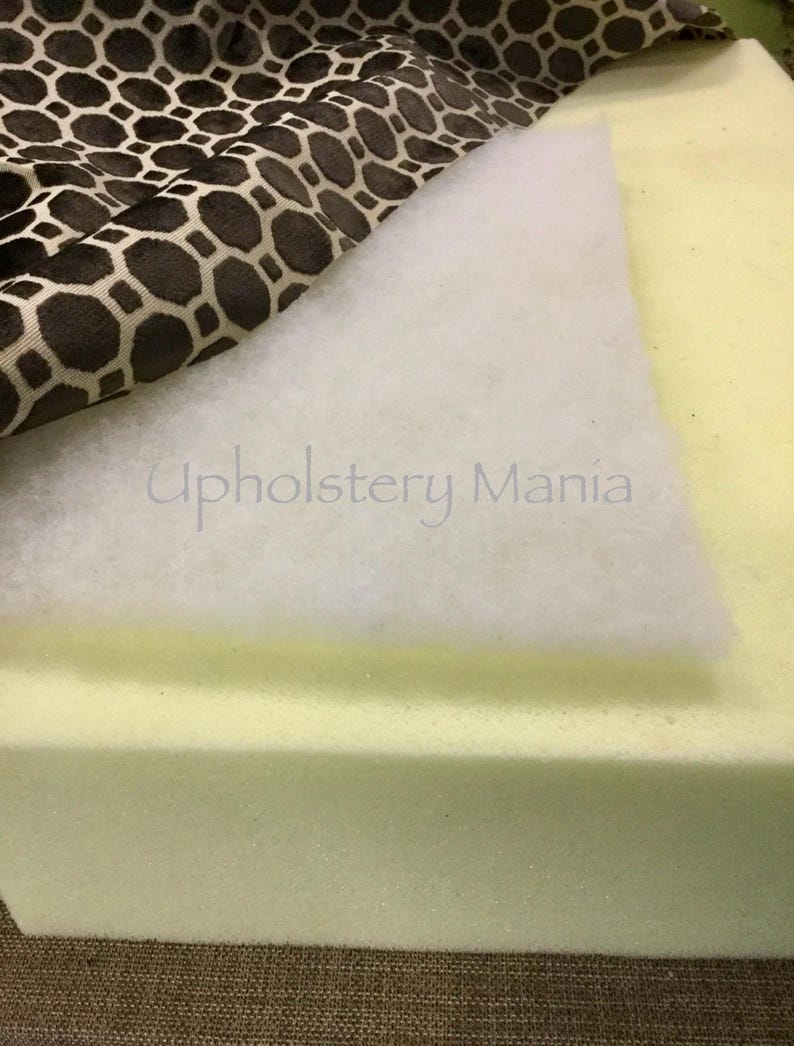 May include: A close-up of upholstery supplies, including a piece of brown and white patterned fabric, a white batting layer, and a thick, light yellow foam cushion. The text "Upholstery Mania" is visible in the image.
