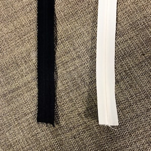 May include: Two zipper tapes, one black and one white, are shown against a brown burlap background.