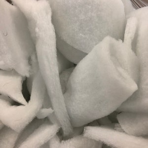 May include: Close-up of a pile of white polyester fiberfill. The fiberfill is soft and fluffy, with various shapes and sizes. The material is used for stuffing pillows, cushions, and other craft projects.