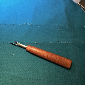 May include: A close-up of a seam ripper with a wooden handle on a teal fabric surface.