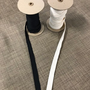 May include: Two spools of elastic, one black and one white, are unwinding on cardboard spools. The elastic is a common sewing and crafting supply.