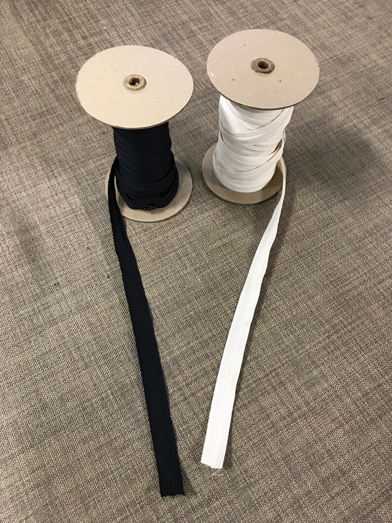 May include: Two spools of elastic, one black and one white, are unwinding on cardboard spools. The elastic is a common sewing and crafting supply.