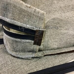 May include: Close-up of a gray fabric with a black zipper and brown leather trim. The fabric is sewn with white thread.