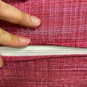 May include: Close-up of a red fabric with a white zipper. The fabric has a textured, woven appearance.
