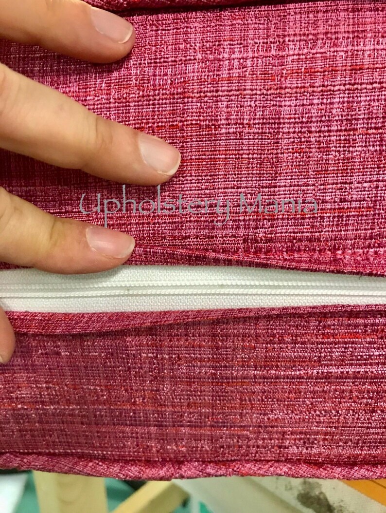 May include: Close-up of a red fabric with a white zipper. The fabric has a textured, woven appearance.