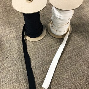 May include: Two spools of zipper tape, one black and one white, are wound around cardboard spools. The spools are sitting on a brown fabric surface.