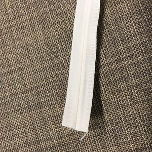 May include: White zipper tape for sewing projects. The tape is about 1/2 inch wide and has a smooth finish.