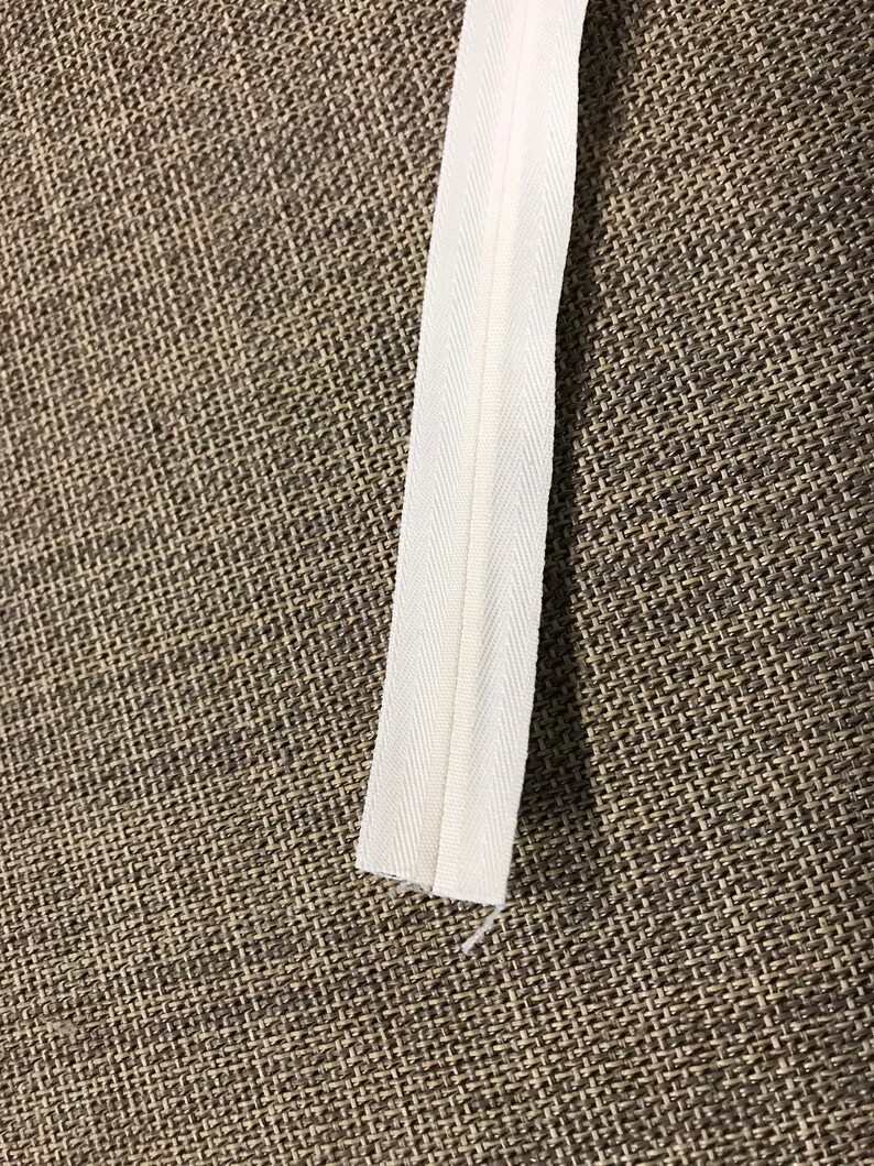 May include: White zipper tape for sewing projects. The tape is about 1/2 inch wide and has a smooth finish.
