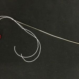 May include: A red ball with a white thread wrapped around it, with a long, thin needle extending from the ball.