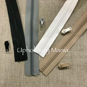 May include: Four different types of zipper tape, including black, gray, white, and beige. The zipper tape is laid out on a beige fabric background. The text "Upholstery Mama" is visible in the center of the image.