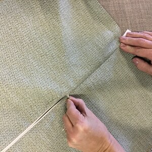 May include: A close-up of a person's hands sewing a zipper into a light green fabric cushion cover.