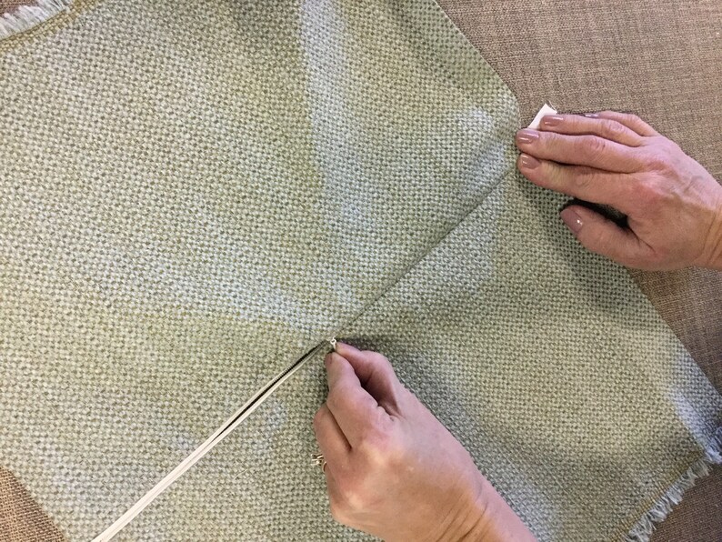 May include: A close-up of a person's hands sewing a zipper into a light green fabric cushion cover.