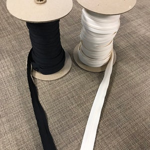 May include: Two spools of zipper tape, one black and one white, are unwinding on cardboard spools. The zipper tape is laying on a brown textured surface.