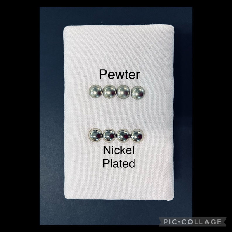 May include: A white fabric square displays two sets of four small, round, metallic objects. The top row is labelled "Pewter," and the bottom row is labelled "Nickel Plated." The objects are likely buttons or decorative elements.