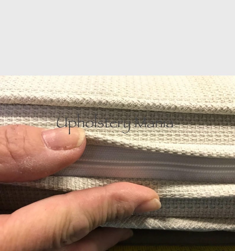 May include: Close-up of a beige fabric with a zipper. The fabric is folded over to show the zipper. The zipper is white and has a metal slider.