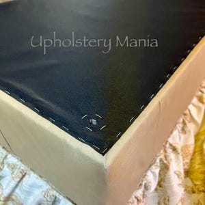 May include: Close-up of a beige upholstered box with black fabric on top. The fabric is stitched around the edges of the box. The text "Upholstery Mania" is visible on the fabric.