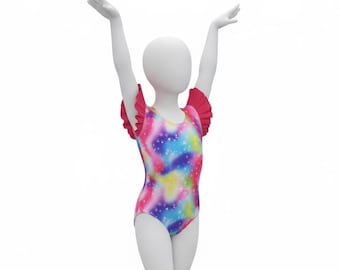 Puede incluir: Un leotardo sin mangas con un vibrante estampado de galaxia multicolor y patrones de estrellas blancas. La prenda incluye mangas cortas con volantes en color rosa sólido y un escote redondo, exhibido en un maniquí blanco con brazos alzados.