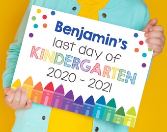 May include: A white sign with colourful crayon drawings at the bottom. The sign says "Benjamin's last day of KINDERGARTEN 2020 - 2021".