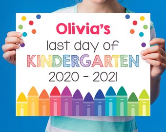 May include: A white sign with colorful crayon accents and the text "Olivia's last day of KINDERGARTEN 2020 - 2021".