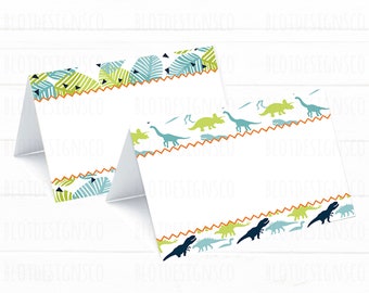 Pode incluir: Dois cartões de lugar imprimíveis com tema de dinossauros. O cartão superior tem um padrão de folhas de palmeira e triângulos verdes, azuis e laranja. O cartão inferior tem uma borda de dinossauros verdes, azuis e laranja.