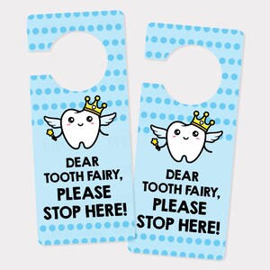 Puede incluir: Un colgador de puerta azul con un diseño de hada de los dientes blanco. El hada de los dientes lleva una corona dorada y alas. El texto en el colgador dice "Querida hada de los dientes, por favor, ¡detente aquí!"