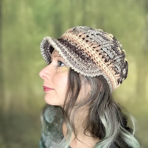 May include: A crocheted hat with a wide brim in shades of brown, beige, and peach. The hat is made with a textured stitch and has a slouchy fit.