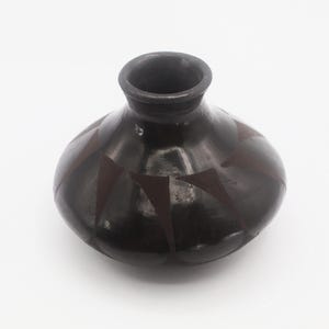 May include: A dark brown, round ceramic vase with a narrow neck. The vase features a geometric pattern of dark red triangles. The vase is likely handmade and suitable for home decor.