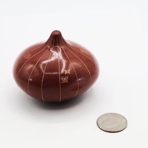 May include: A brown, onion-shaped decorative object with etched lines and butterfly designs. The object is next to a quarter coin for size comparison. The object is likely ceramic or pottery.