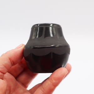May include: A small, black, hand-painted pottery vase with a geometric design. The vase is made by a Native American artist.