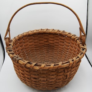 May include: A large, round, brown woven basket with a single handle. The basket is made of natural materials and has a rustic appearance.