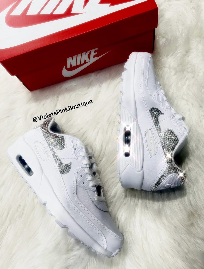 May include: White leather Nike Air Max 90 sneakers with a silver rhinestone swoosh and a white Nike box. The text '@VioletsPinkBoutique' is visible on the box.