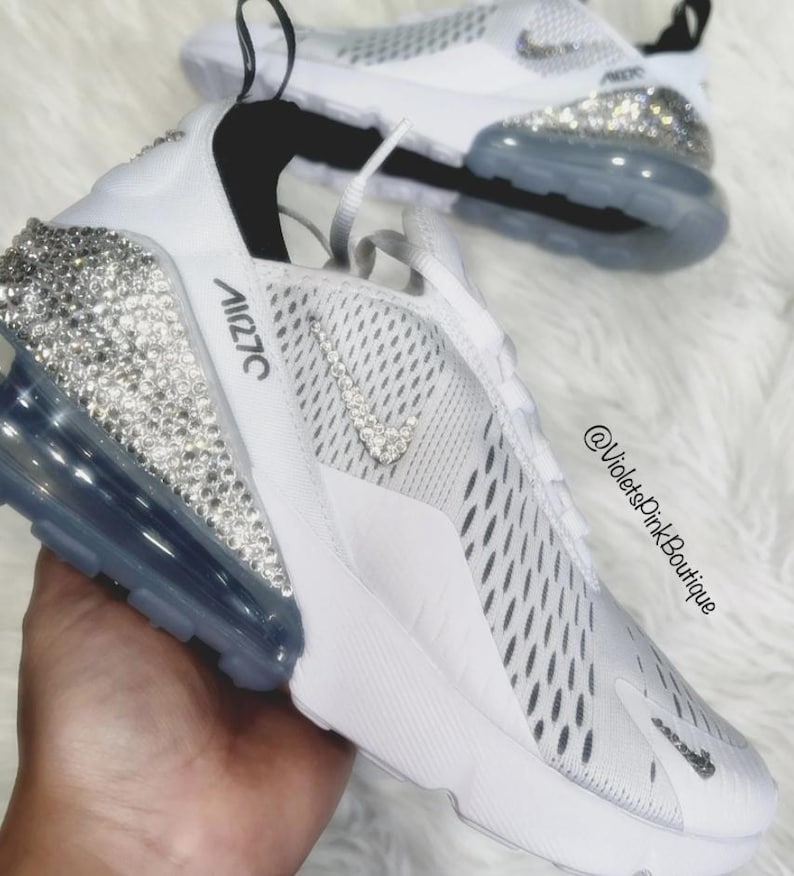 Puede incluir: Zapatillas deportivas blancas con adornos de cristal en el tal&oacute;n y el logotipo de Nike. Las zapatillas tienen una suela blanca y una burbuja de aire gris. El texto "Air 270C" est&aacute; impreso en el lateral.