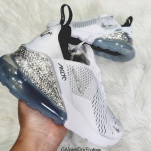 Puede incluir: Zapatillas deportivas blancas con adornos de cristal. Las zapatillas presentan una parte superior de malla blanca, un tal&oacute;n cubierto de cristal y una suela transparente. El logotipo de Nike es visible en el lateral. El texto "Air 270" est&aacute; impreso en el lateral.