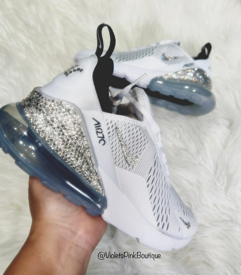 Puede incluir: Zapatillas deportivas blancas con adornos de cristal. Las zapatillas presentan una parte superior de malla blanca, un tal&oacute;n cubierto de cristal y una suela transparente. El logotipo de Nike es visible en el lateral. El texto "Air 270" est&aacute; impreso en el lateral.