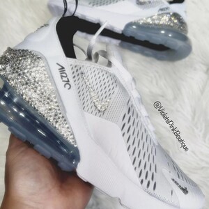 Puede incluir: Zapatillas deportivas blancas con adornos de cristal en el tal&oacute;n y el logotipo de Nike. Las zapatillas tienen una suela blanca y una burbuja de aire gris. El texto "Air 270C" est&aacute; impreso en el lateral.