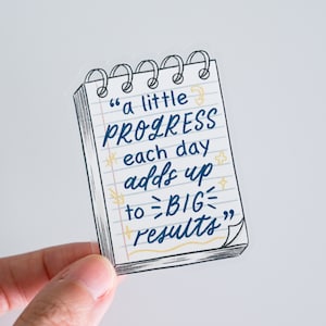 Könnte beinhalten: Ein Aufkleber in Form eines Notizblocks mit dem Zitat "a little PROGRESS each day adds up to BIG results" in Blau und Gelb. Der Notizblock hat eine Spiralbindung und liniertes Papier.