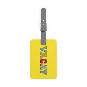 Op de afbeelding: Een gele bagagelabel met het woord "VACAY" in kleurrijke letters. Het label heeft een grijze riem met een zilveren gesp. Het label is rechthoekig en heeft afgeronde hoeken.