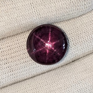 Op de afbeelding: Een diep paarse ster-robijn cabochon edelsteen met een zespuntige ster in het midden.