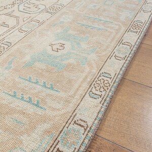 May include: A beige runner rug with a blue and brown geometric pattern. The rug has a fringe border.