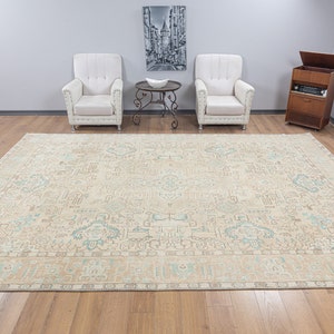 May include: A beige area rug with a light blue and brown patterned design. The rug has a fringe border and is laid out on a hardwood floor.