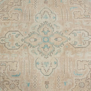 May include: A beige rug with a light blue and brown geometric pattern. The rug has a central medallion with a repeating pattern of four-pointed stars.