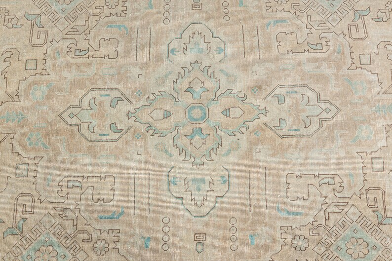 May include: A beige rug with a light blue and brown geometric pattern. The rug has a central medallion with a repeating pattern of four-pointed stars.
