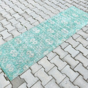 Puede incluir: Una alfombra de pasillo azul turquesa con un patrón floral blanco. La alfombra está colocada en un patio de concreto gris.