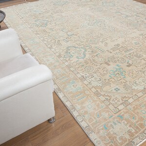 May include: A beige and blue patterned rug with a light brown border. The rug is laid out on a wooden floor with a white armchair in the foreground.