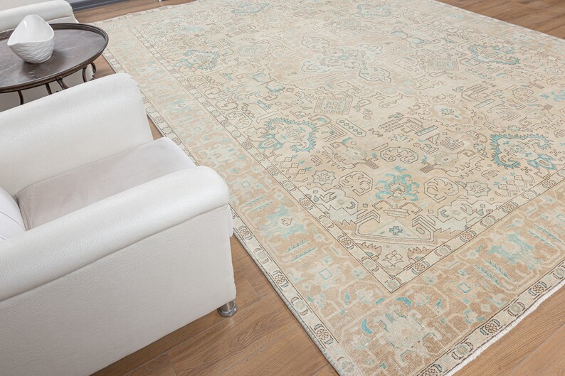 May include: A beige and blue patterned rug with a light brown border. The rug is laid out on a wooden floor with a white armchair in the foreground.